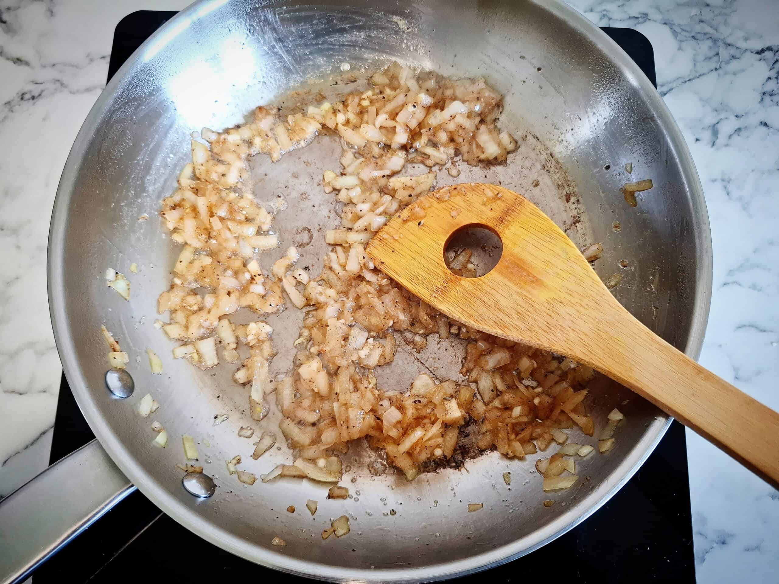 Onions frying until soft in butter in a stainless steel frying pan. Stirring with a wooden spoon