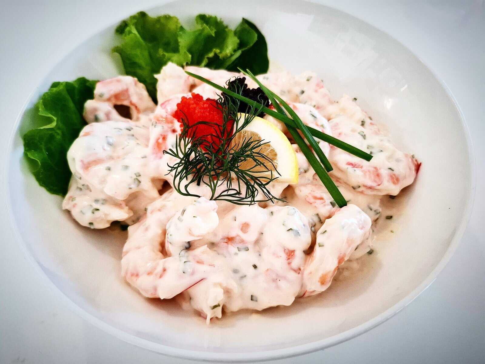 prawn shrimp skagen topped with lump fish caviar, lemon and fresh dill in a white bowl garnished with lettuce leaves and fresh chives