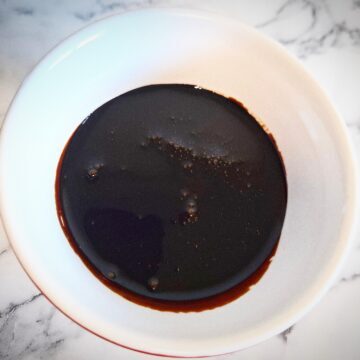 Teriyaki sauce marinade in a white and red ramekin on a marbled bench top