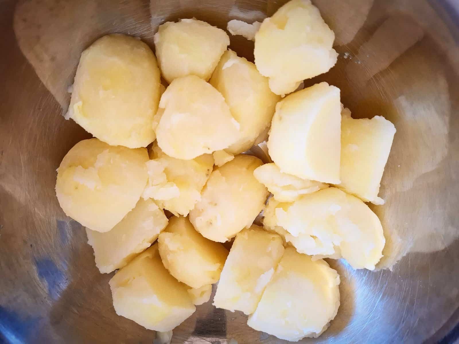 Cooked potatoes cut into pieces in a stainless steel bowl