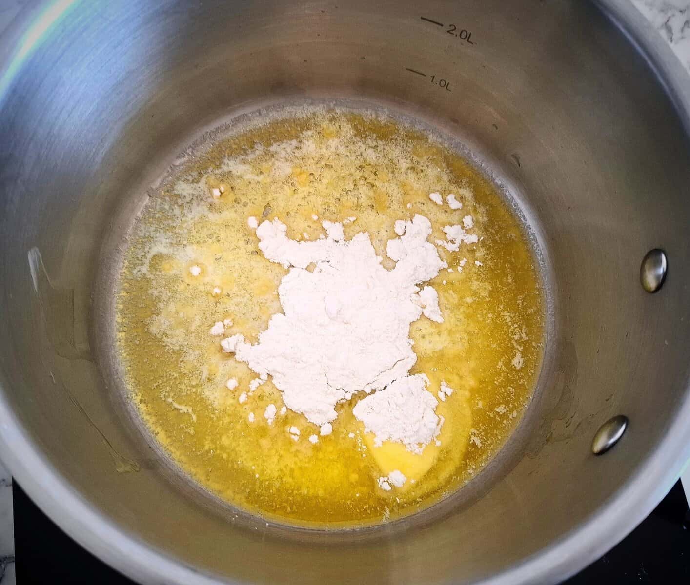 Melted butter with flour sprinkled on top of it in a stainless steel saucepan