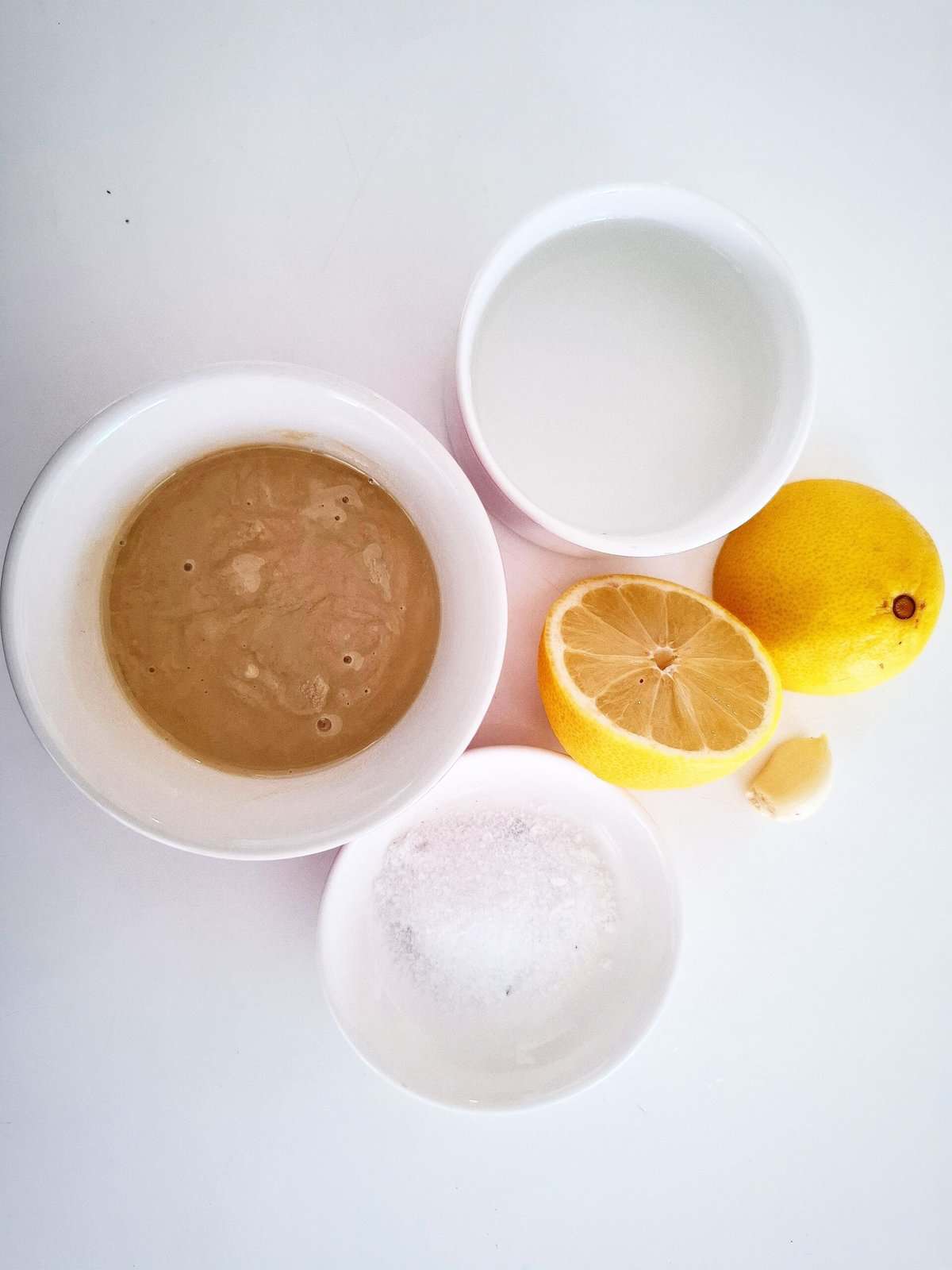Ingredients for sesame, lemon garlic dressing in ramekins on a white background