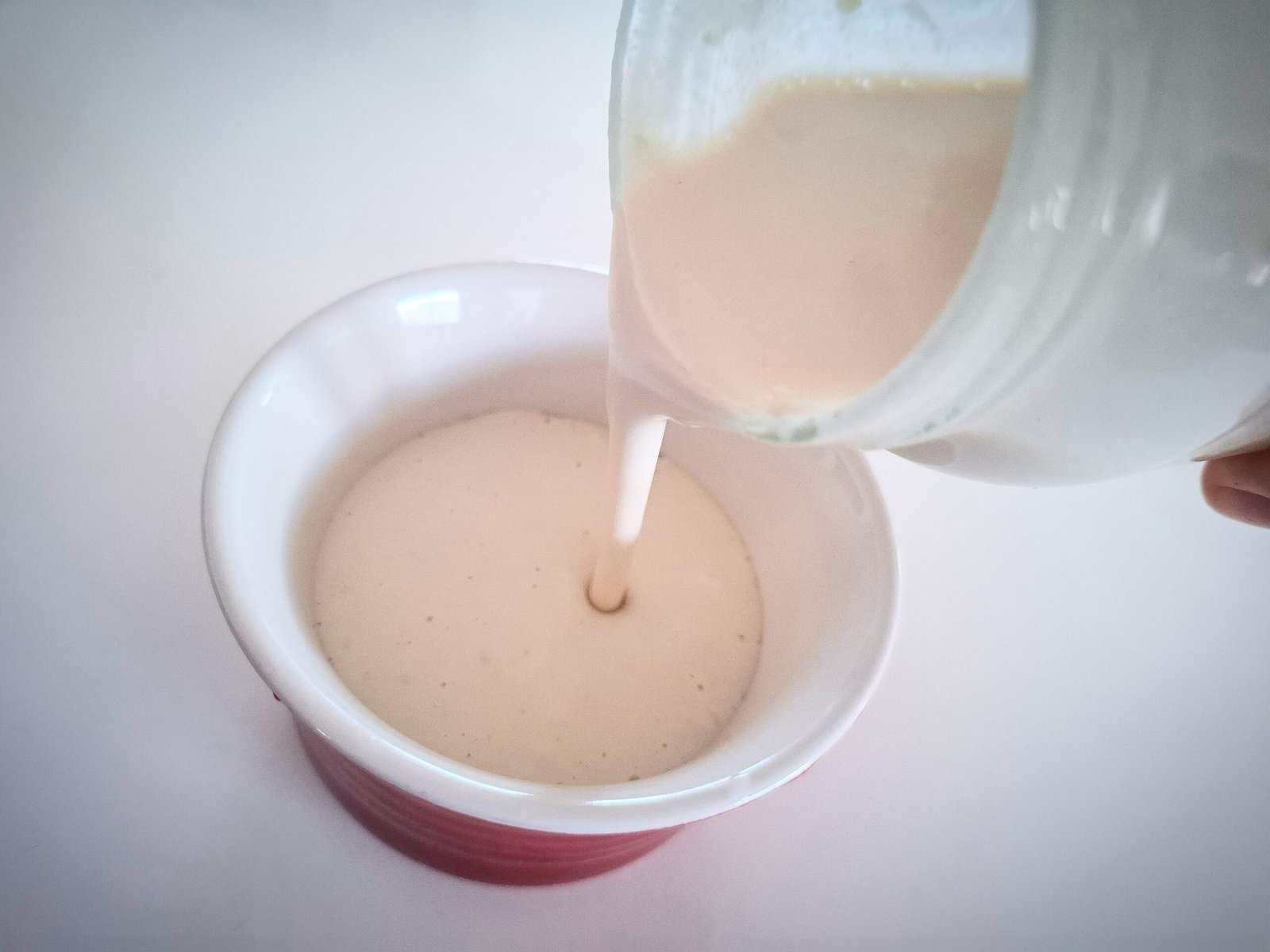 Pouring lemon sesame dressing from a glass jar into a white ramekin on a white table top