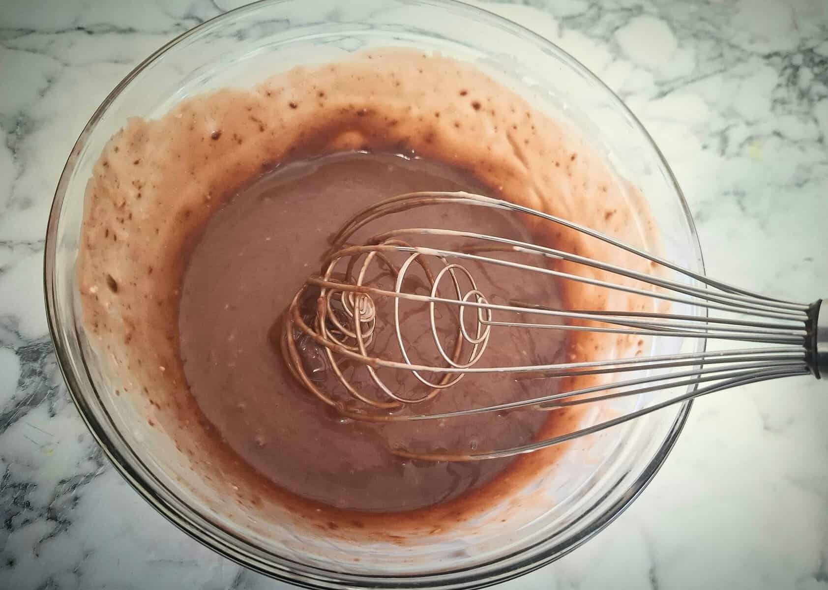 Whisking the cream and chocolate together in a glass bowl on a marbled bench top