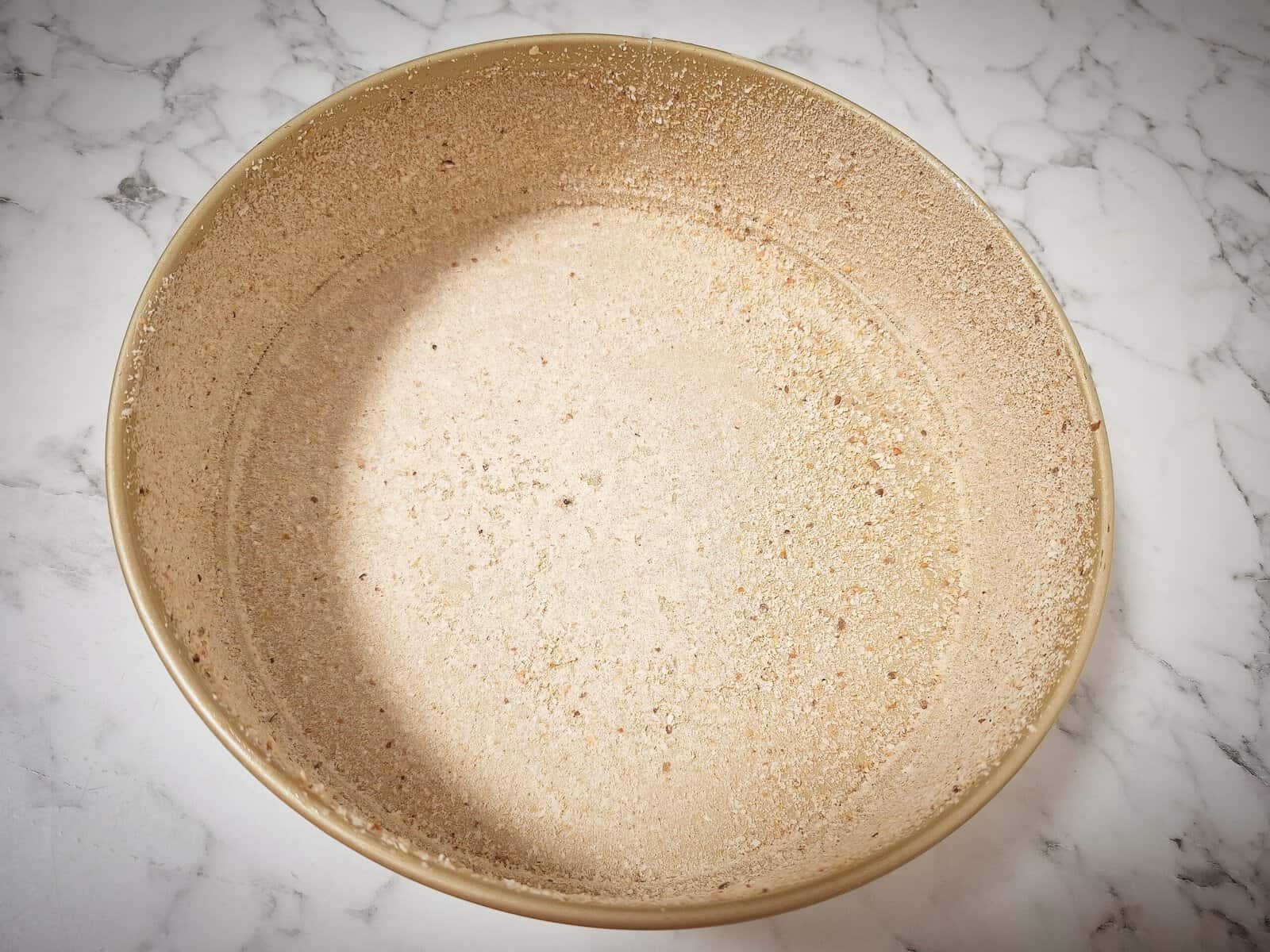 A round cake tin with a thin coating of bread crumbs on the inside of it.