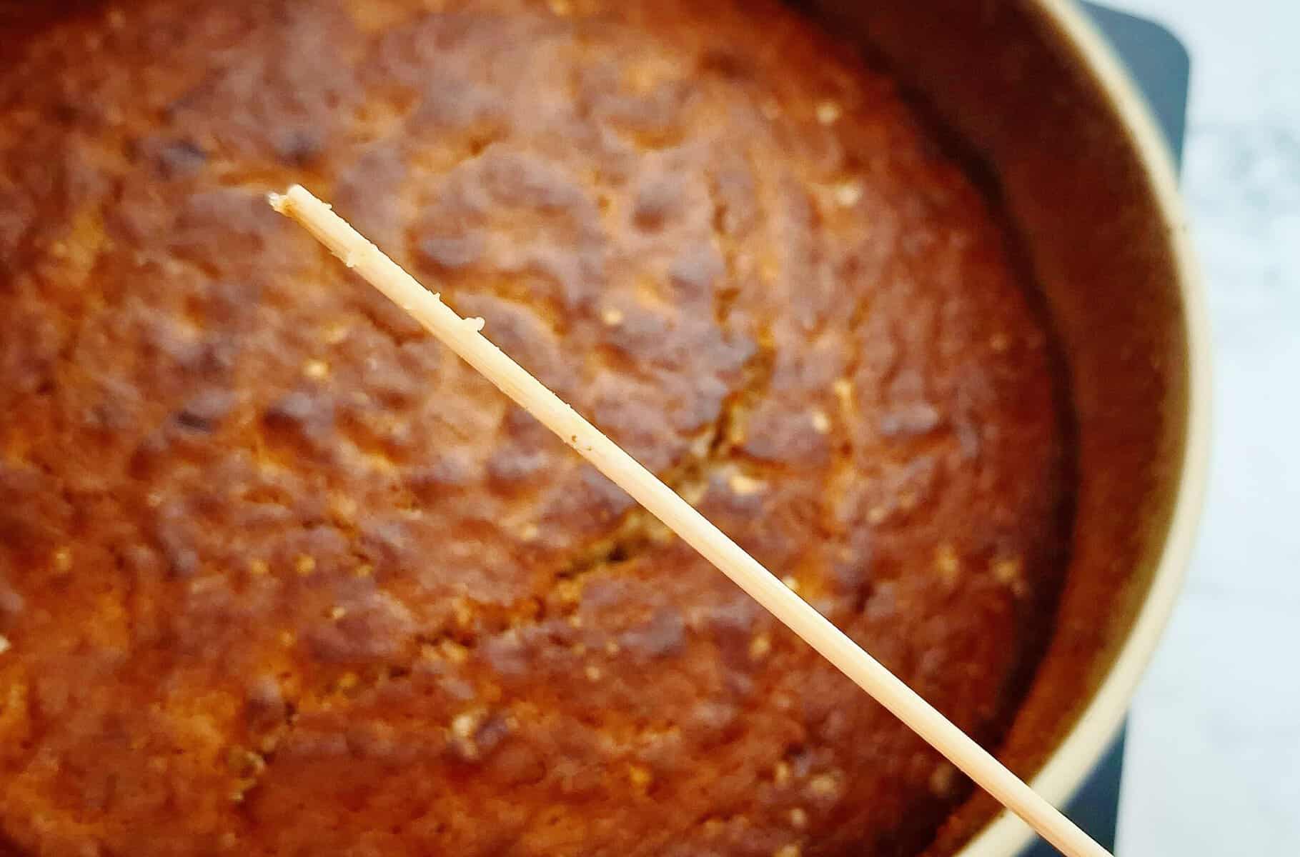 Cooked banana cake and a wooden skewer above it with a few cake crumbs on it.