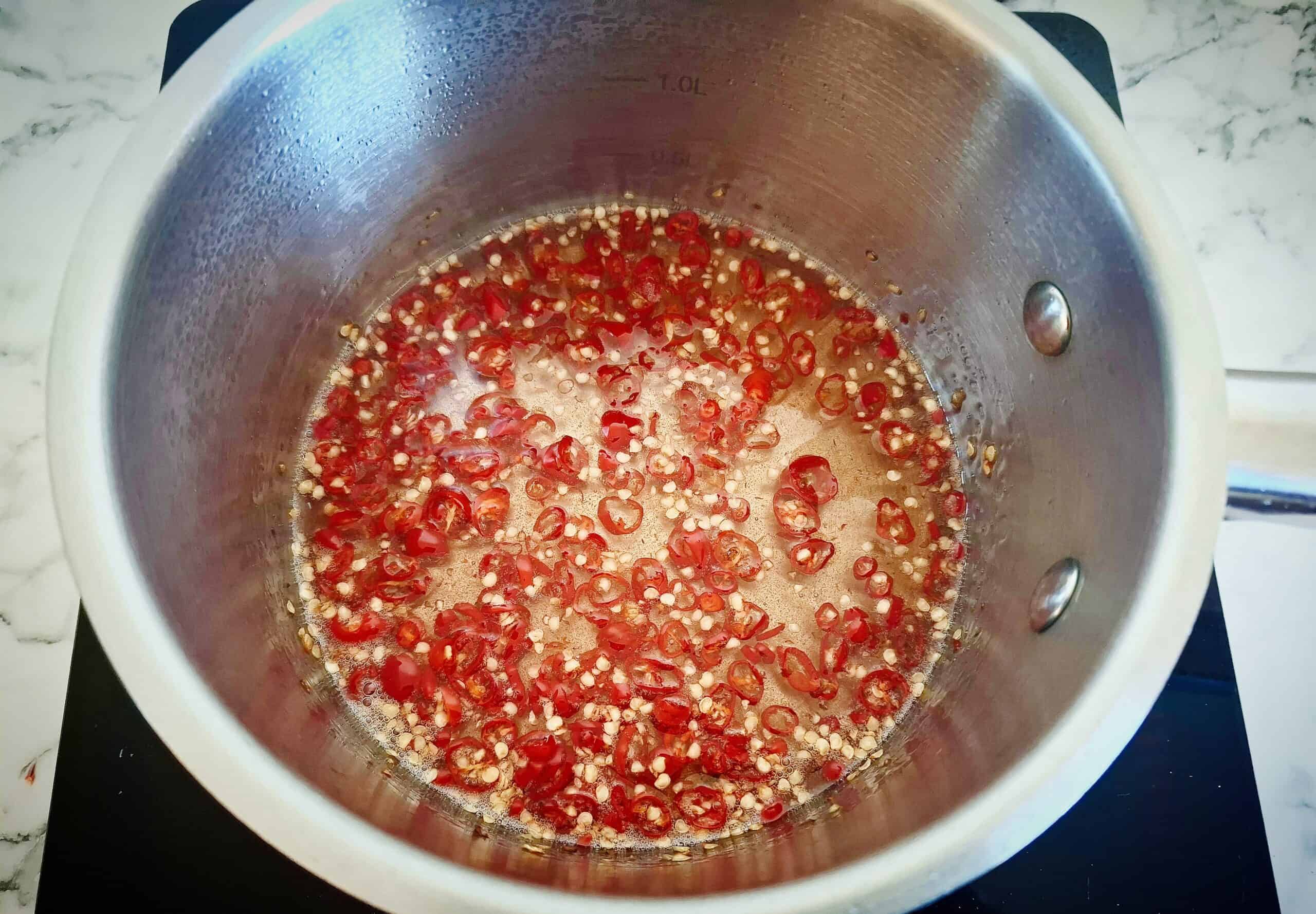 Sliced red chili has been added to a sugar syrup in a sauce pan