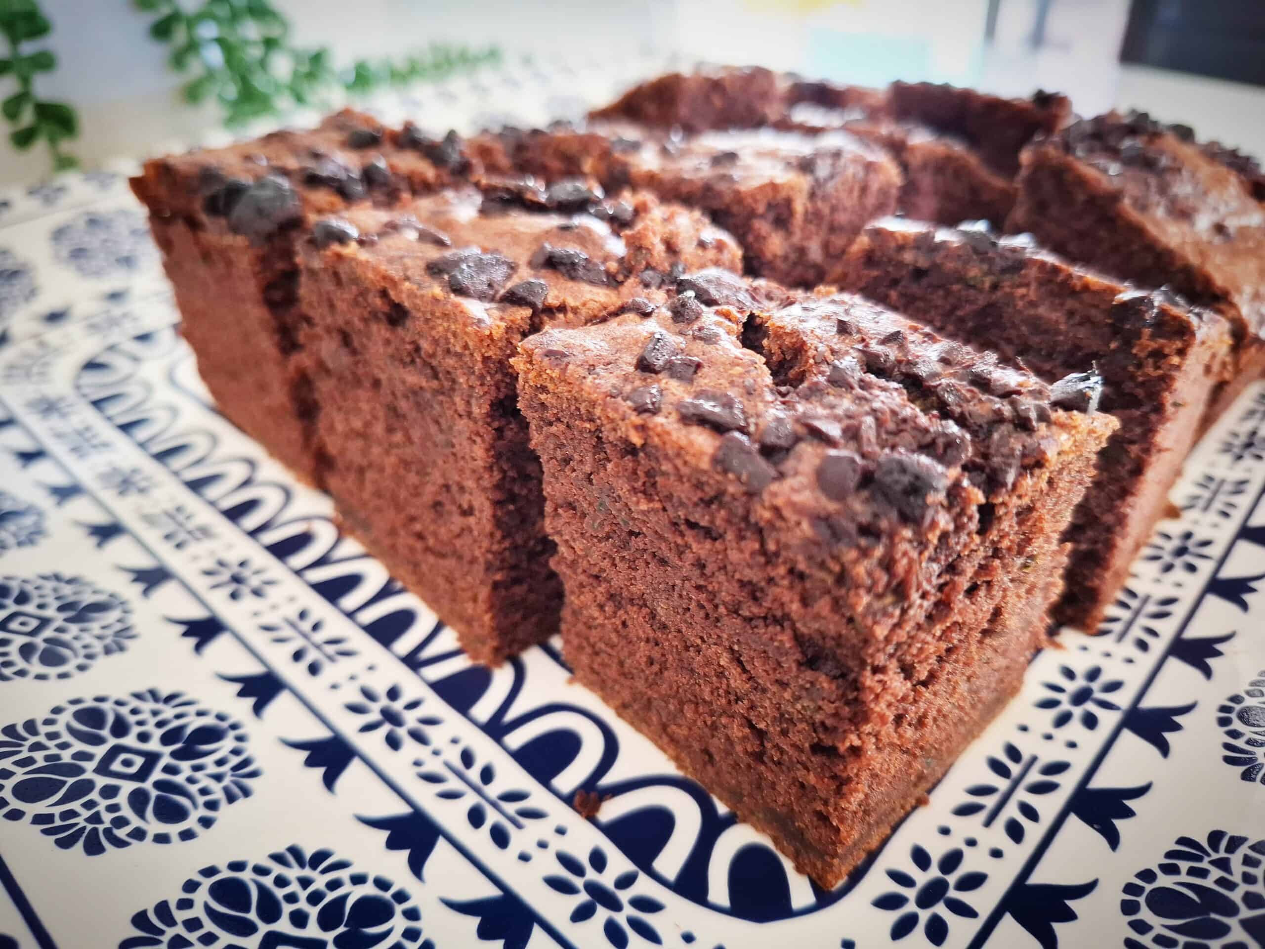 Courgette and chocolate cake cut into square pieces served on a blue and white platter