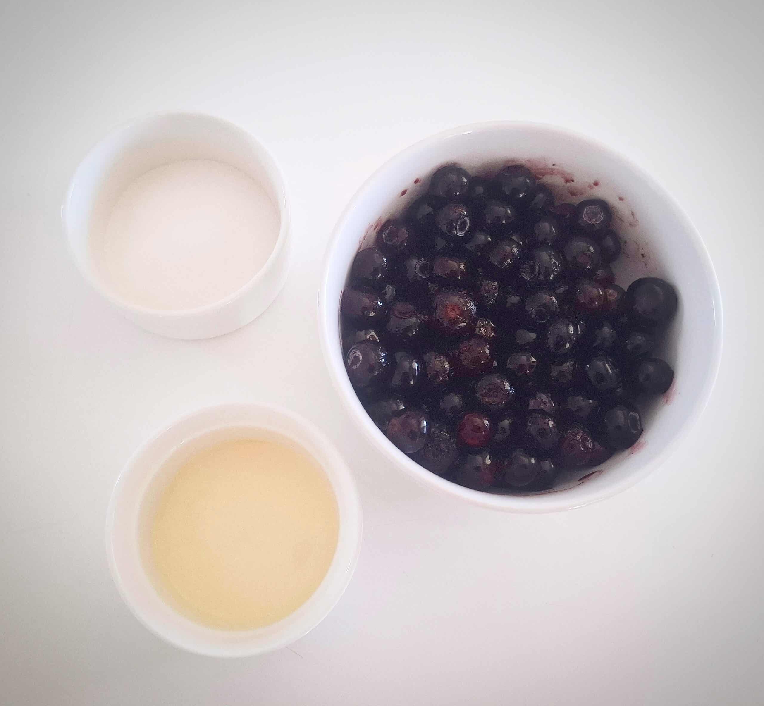 Ingredients for blueberry sauce in ramekins on a white table.