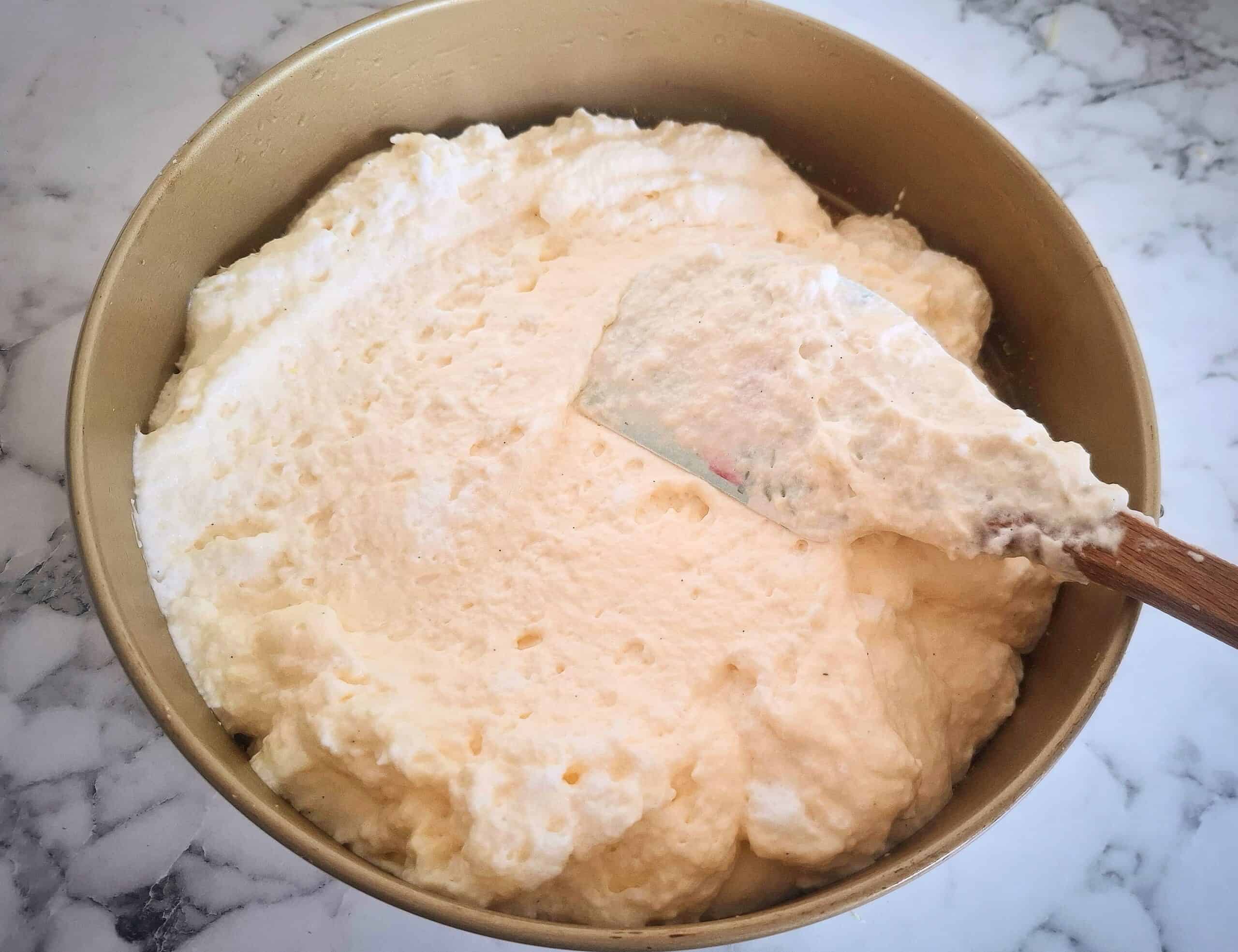 Cheese cake mixture spread out on top of the digestive biscuit crumbs in a round cake tin.