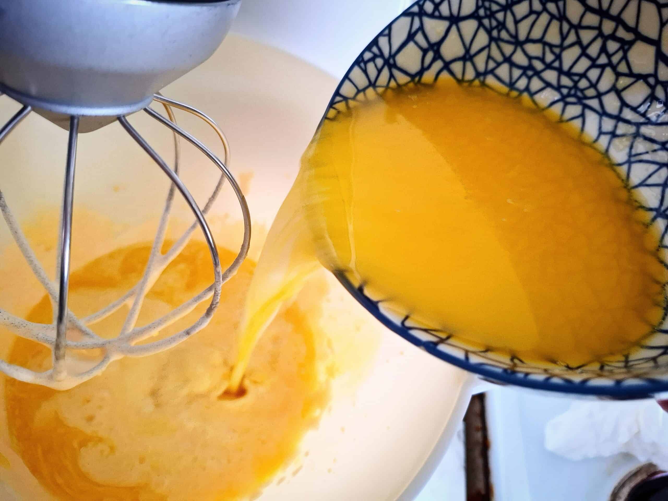 Adding milk and melted butter to the egg and sugar mixture in a white kitchen mixer bowl.