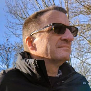Man wearing sunglasses on narrowboat, enjoying outdoor scenery.
