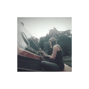 Woman playing piano on narrowboat with trees in background.