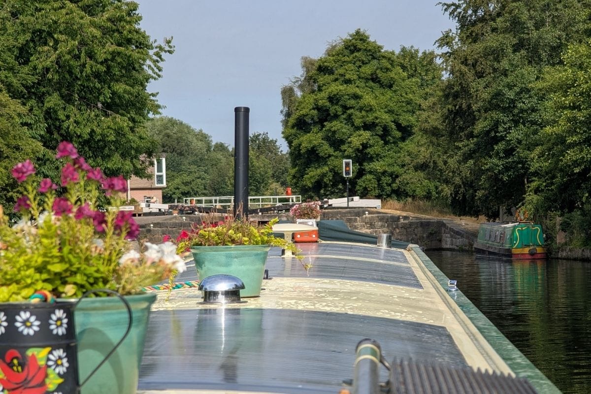 Narrowboat on canal with potted flowers and lush green trees.