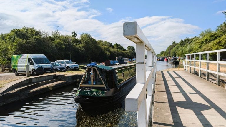 Narrowboat moored on canal with parking and trees in the background.