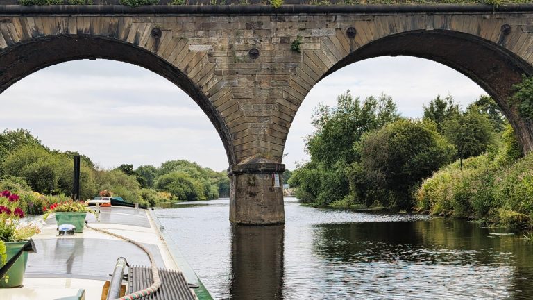 Narrowboat cruising under historic stone bridge on UK river.