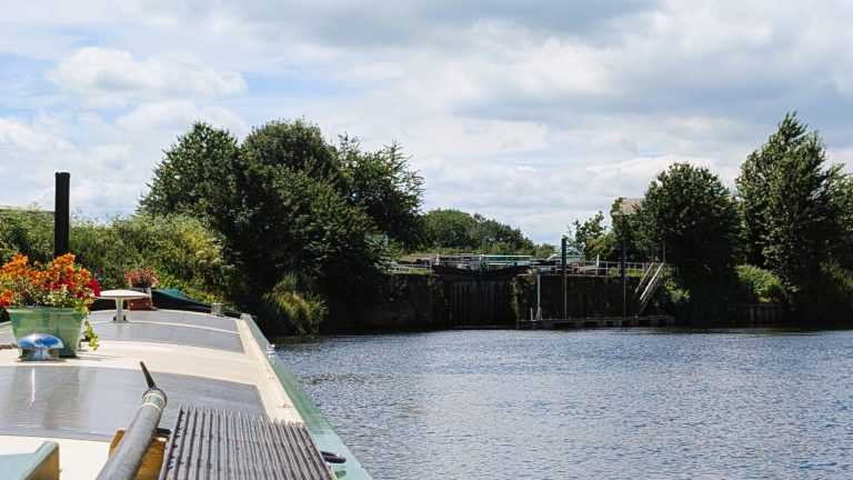 Narrowboat cruising on a peaceful canal surrounded by trees and blue sky.