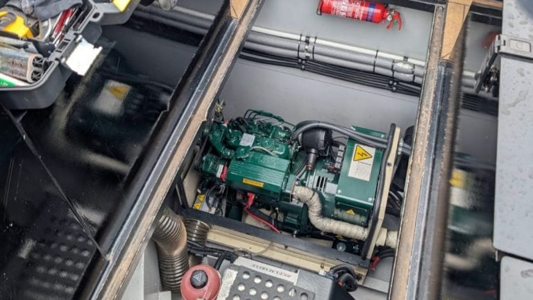 Close-up of a narrowboat engine with green components and black pipes inside the engine room.