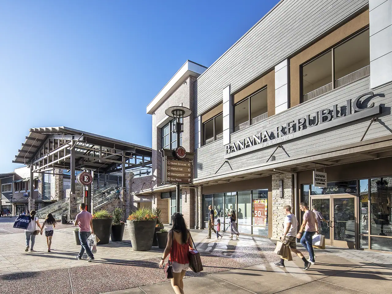 People walking outside Banana Republic store in a shopping mall with clear blue sky.