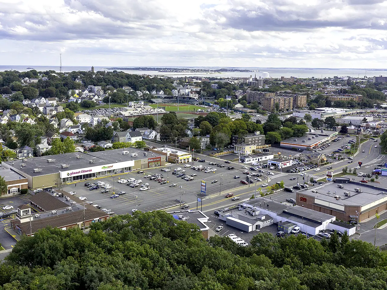 Aerial view of a commercial area with parking lots, retail stores, and surrounding greenery.