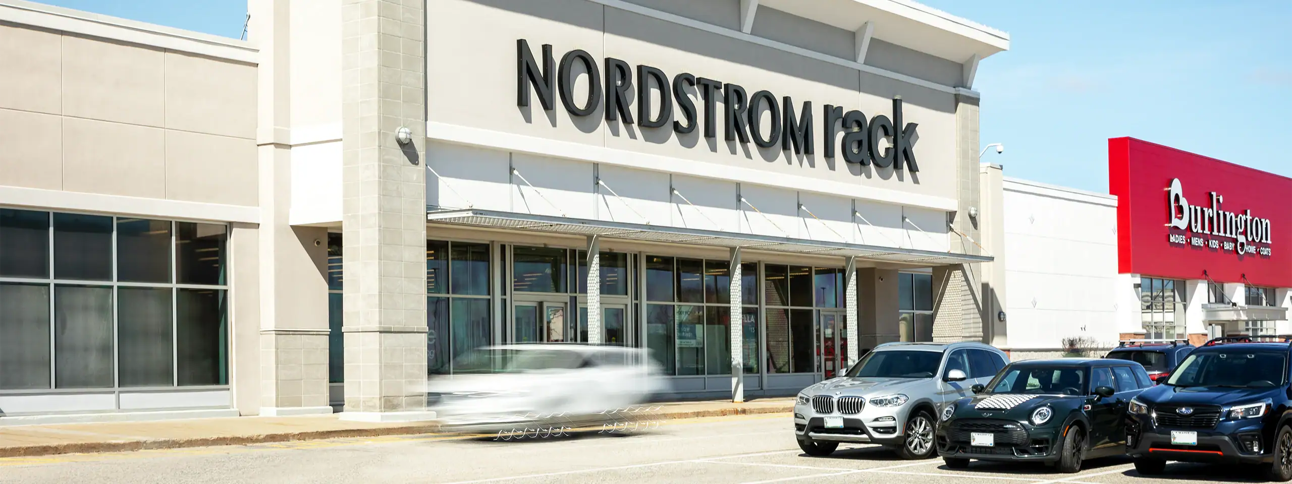 Nordstrom Rack storefront with parked cars in front, located in a shopping center.