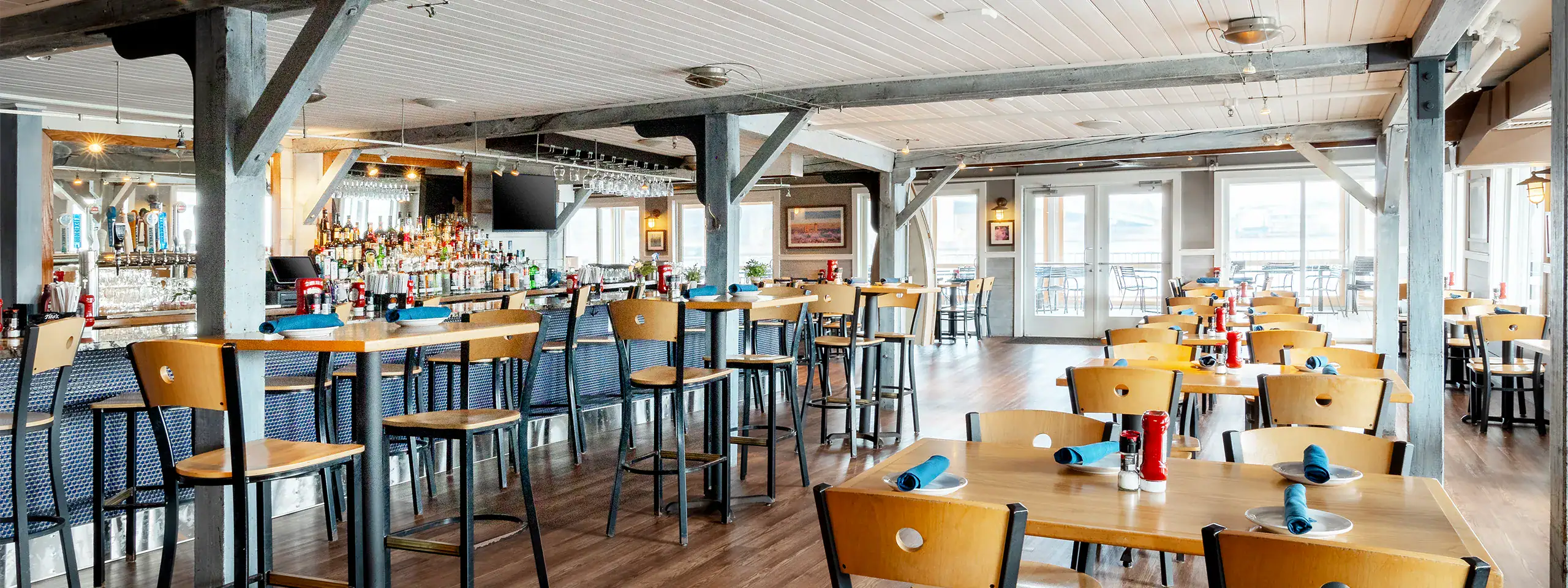 Empty restaurant with wooden tables, chairs, and large windows in New England.
