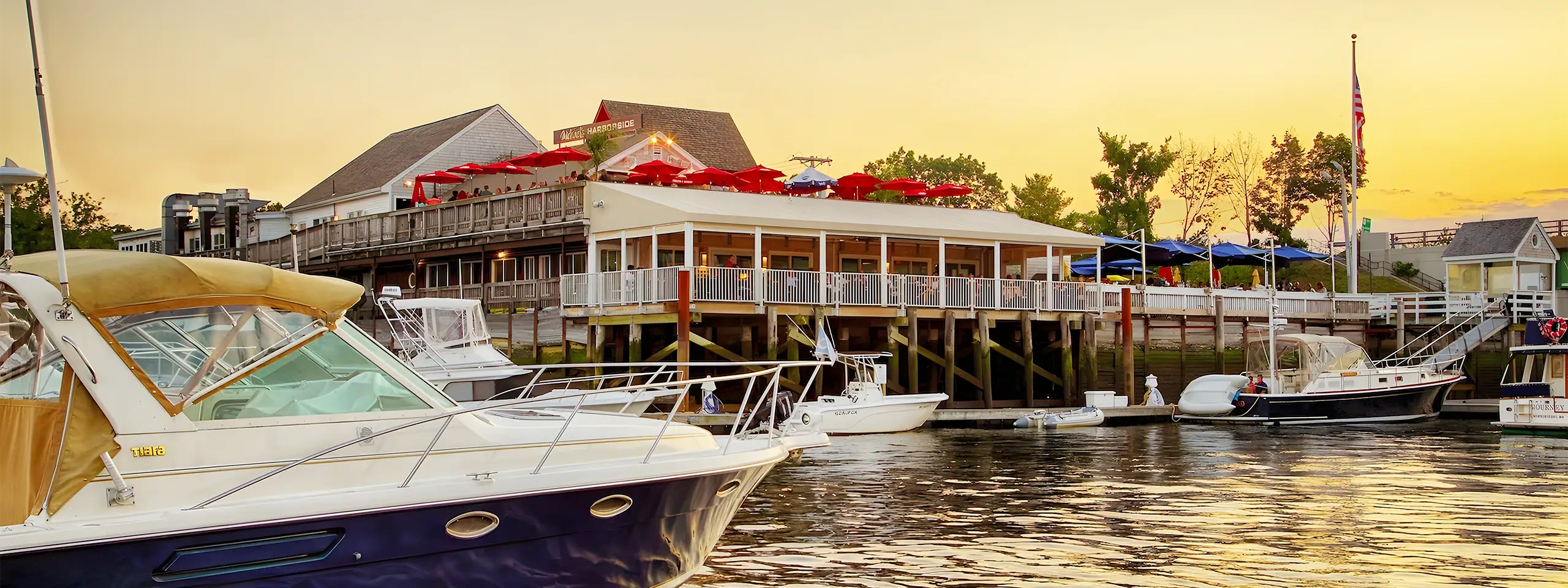 Marina with boats docked and a waterfront restaurant at sunset.