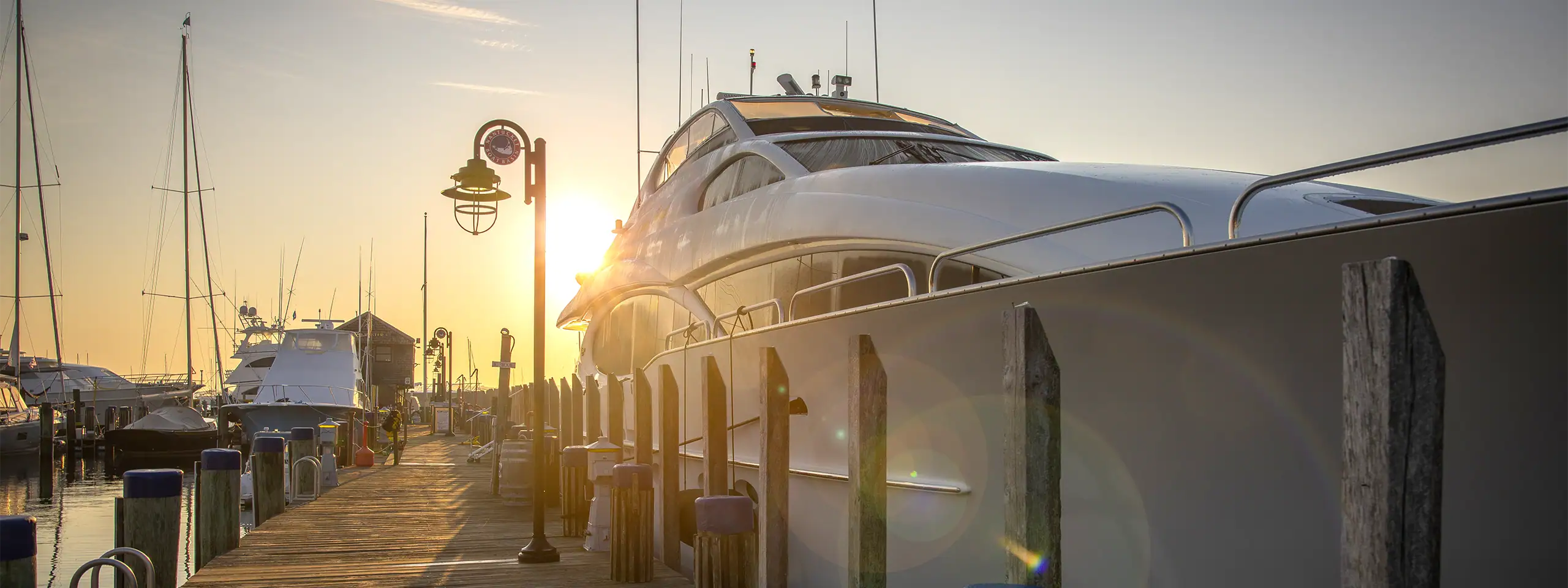 Luxury yacht docked at a marina during sunset with sailboats nearby.