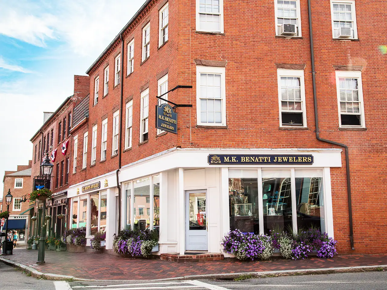 Corner view of M.K. Benatti Jewelers on a brick building with flower planters outside.