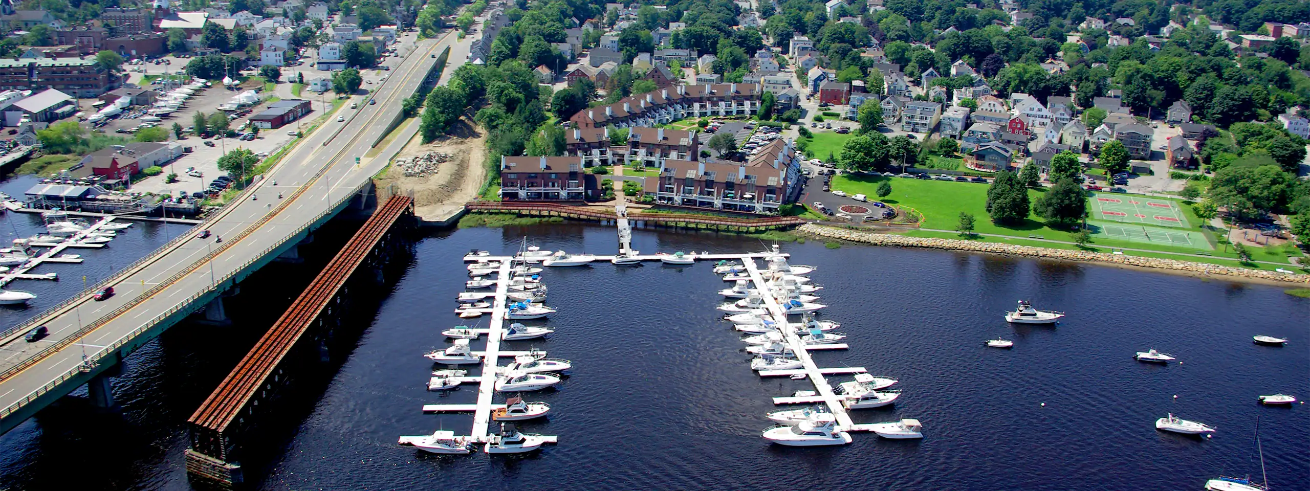 Aerial view of a marina with boats docked on a river in a suburban area.