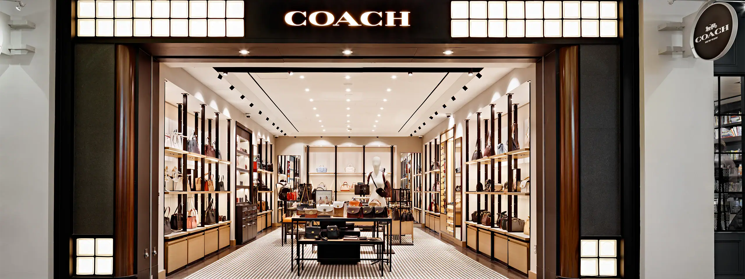 Inside Coach store with shelves of handbags and accessories, modern lighting.
