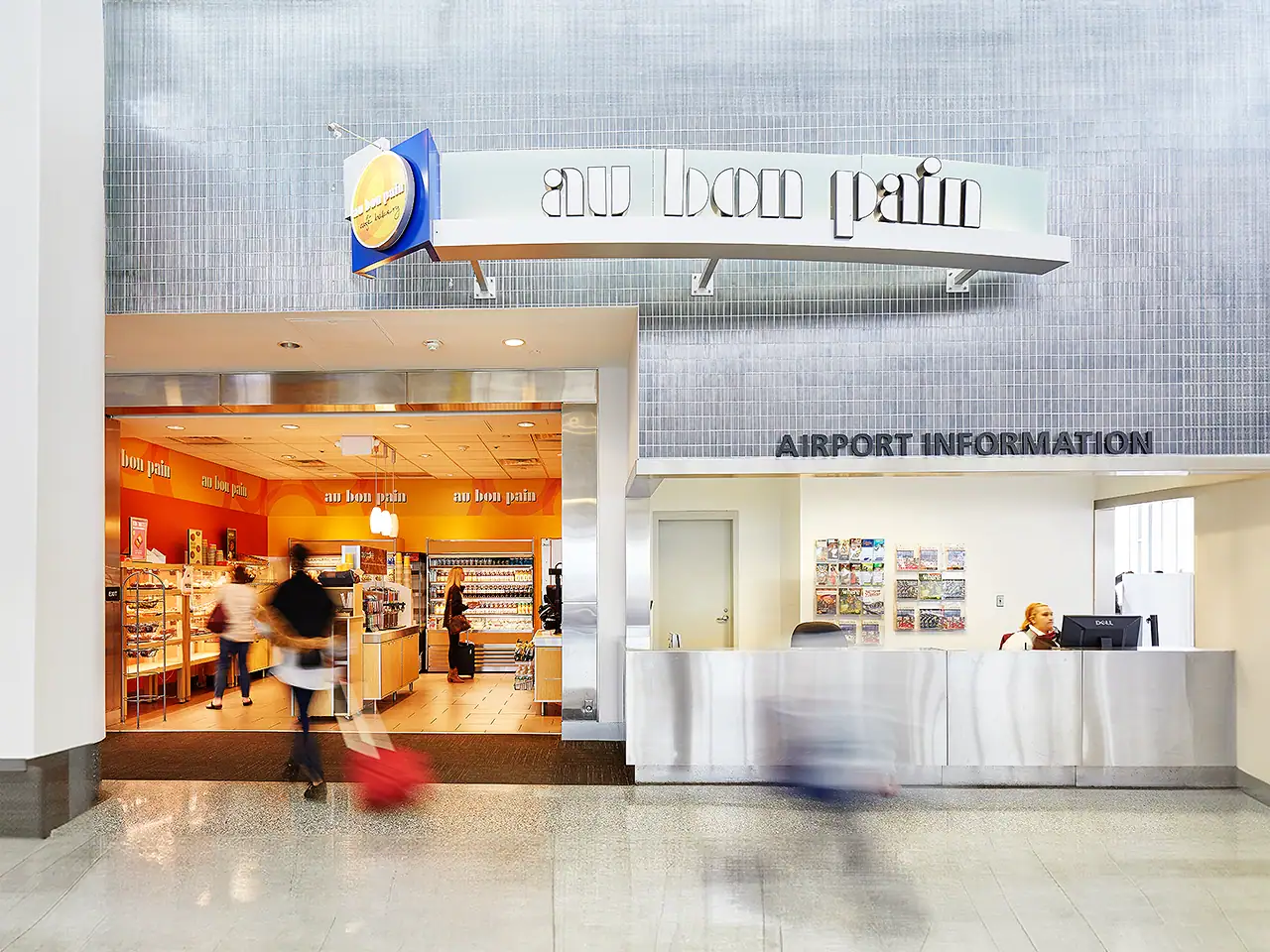 Airport information desk at New England Development property with blurred travelers.