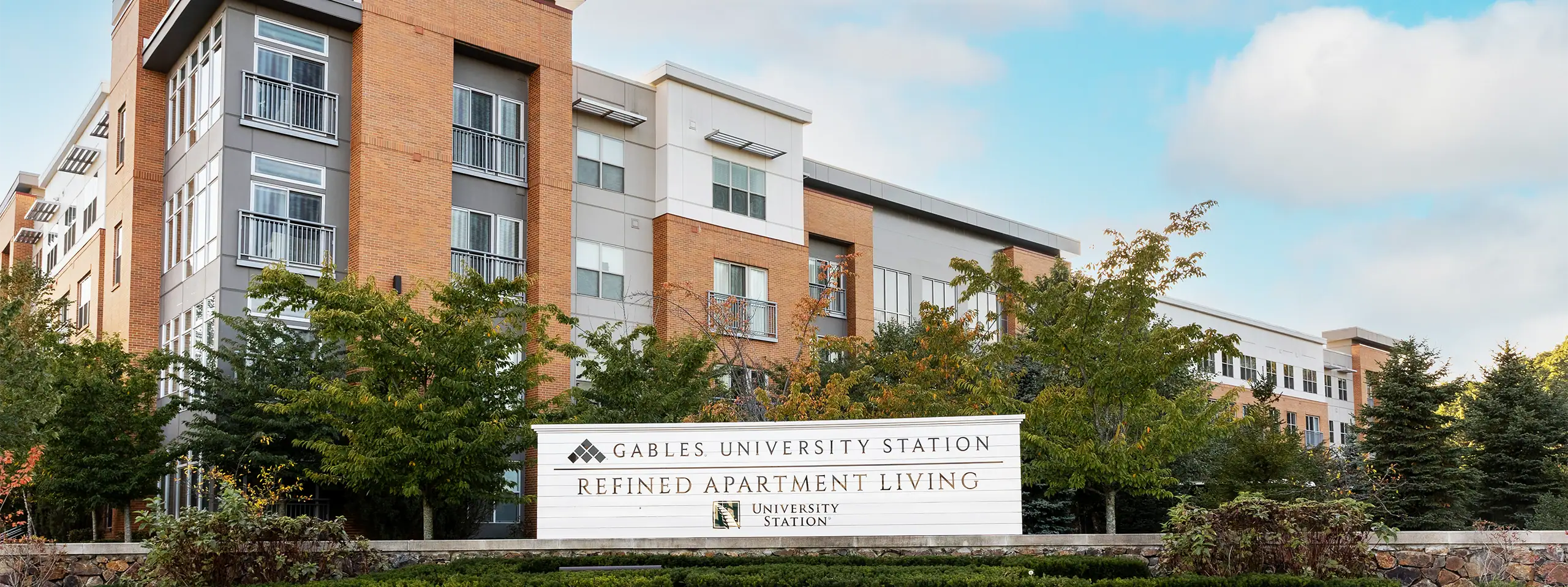 Gables University Station residential apartment building with trees and a sign in front.