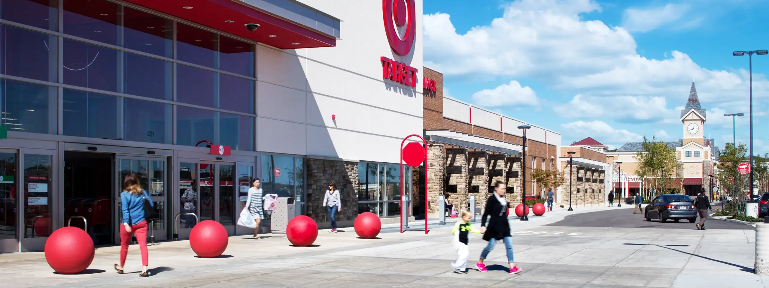 Shoppers walk outside a Target store in a shopping center with a clock tower in the background.