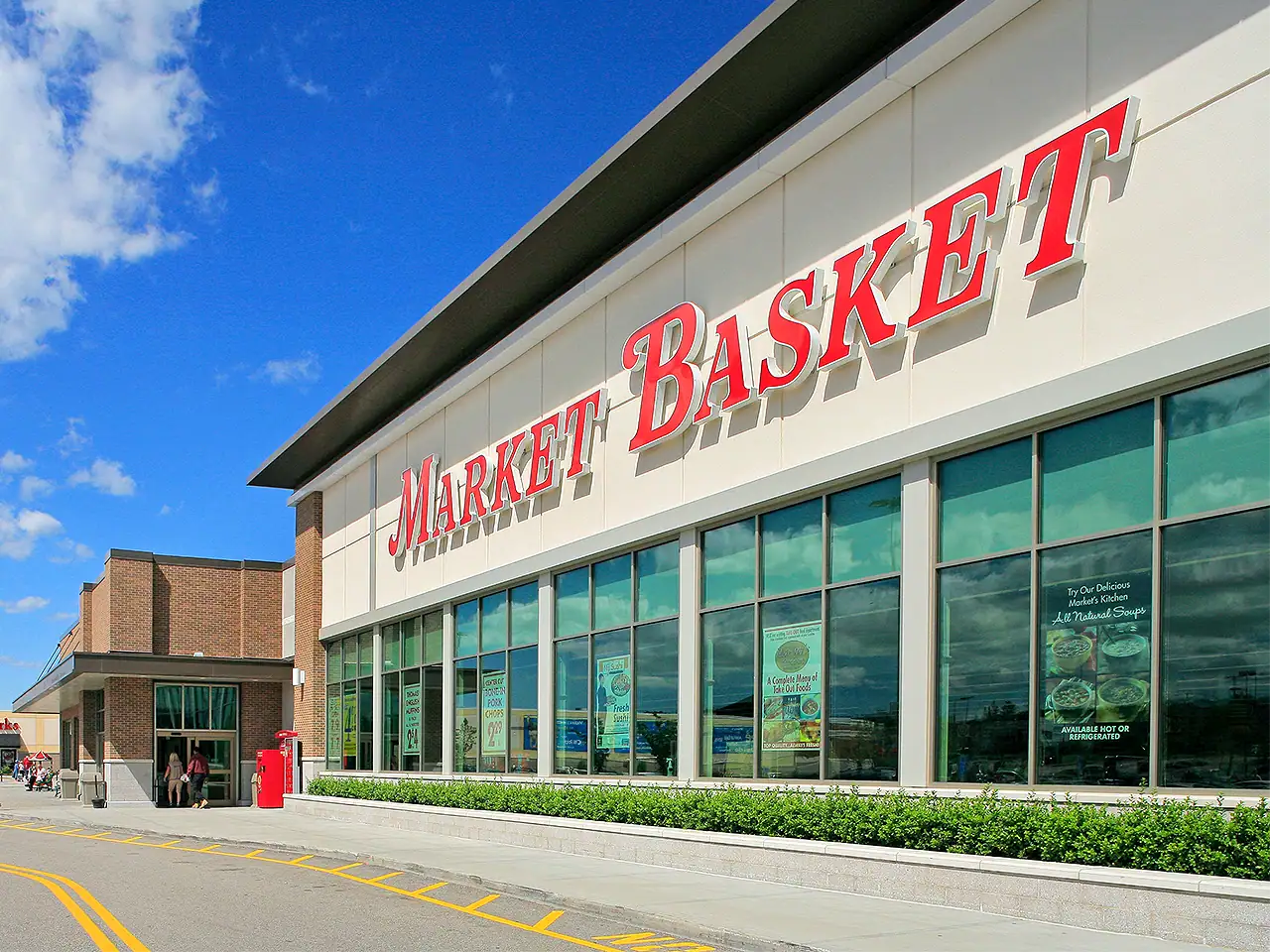 Exterior view of Market Basket grocery store with large glass windows and red signage.