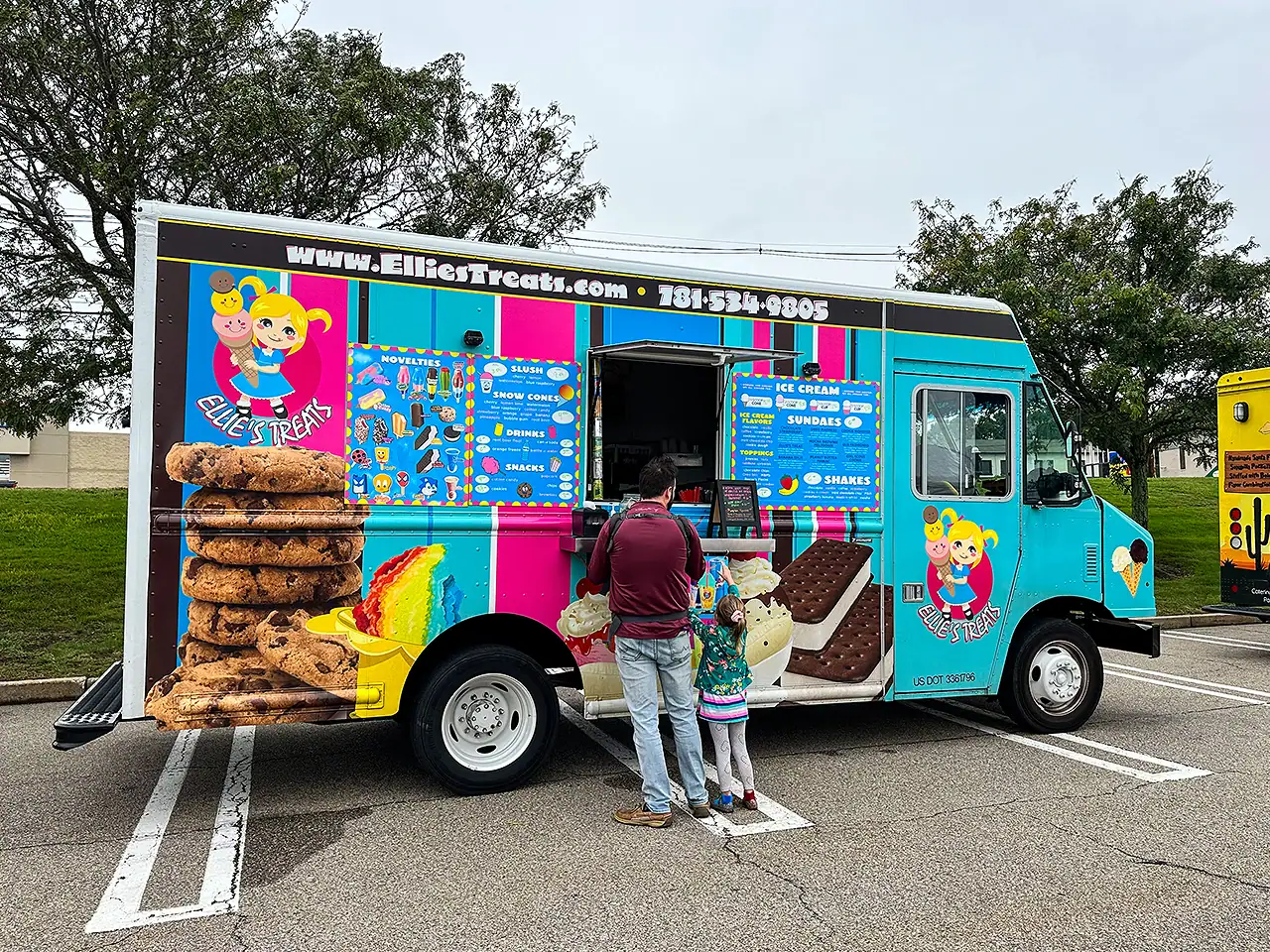 Ellie's Treats ice cream truck with children ordering in a parking lot.