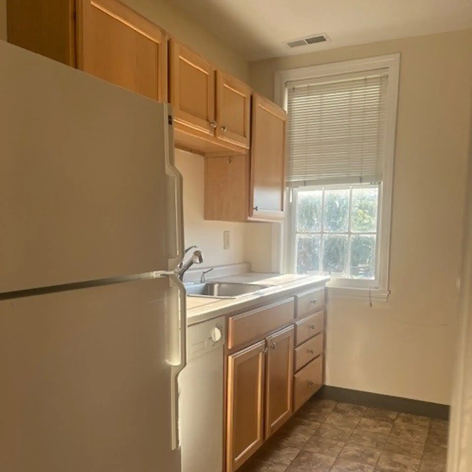 Kitchen with wooden cabinets, a window, and a white refrigerator.