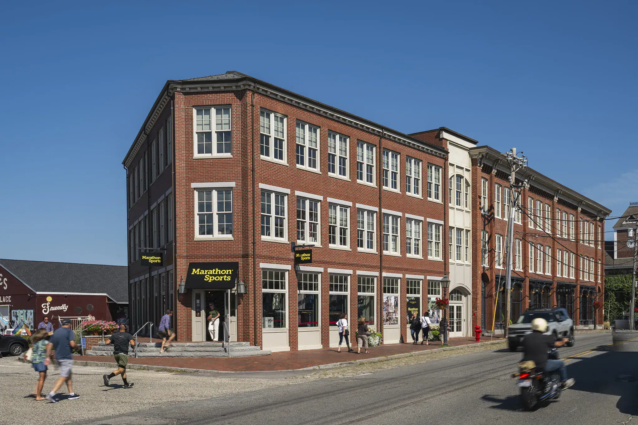 Historic red brick building on a busy street in Newburyport with pedestrians and a motorcycle.