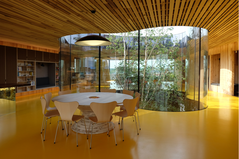 Office interior with large glass windows, wooden accents, and a round table.
