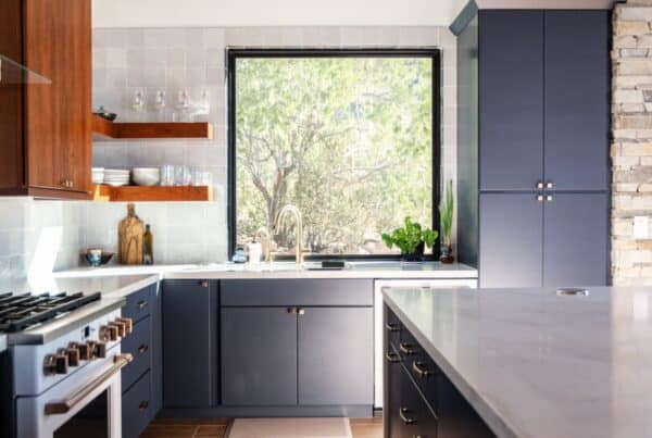 Nu Wavz Homes luxury custom kitchen featuring navy blue lower cabinets, warm wood upper floating shelves, a large picture window over the sink, and a high-end gas range with brass knobs.