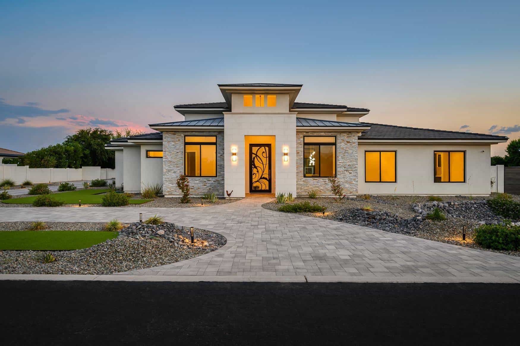 Elegant modern house with large windows and landscaped yard at sunset.