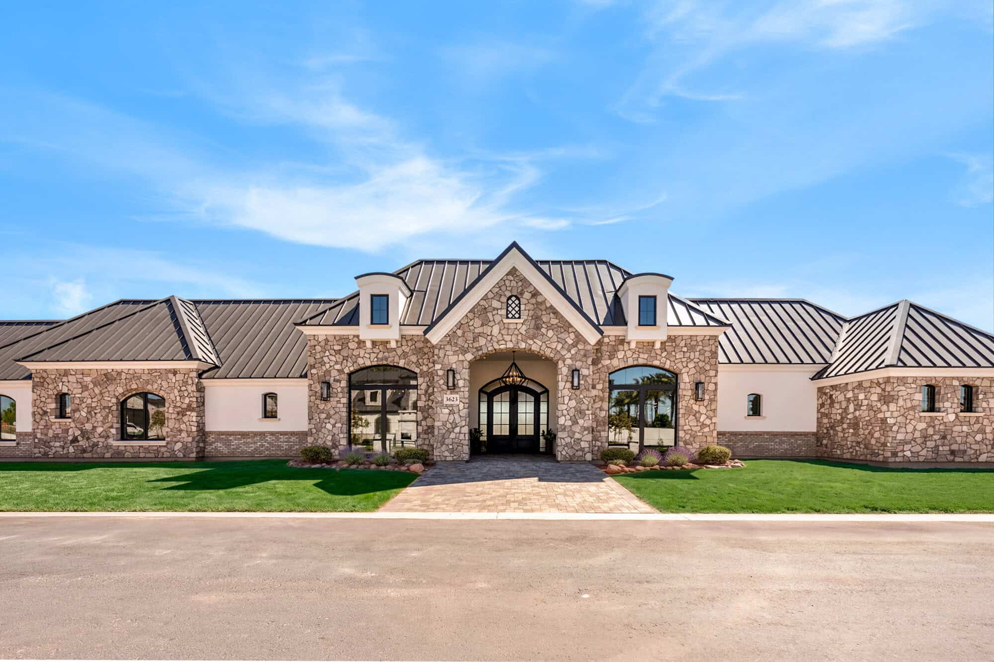 Elegant luxury home with stone and stucco exterior, manicured lawn, under blue sky.