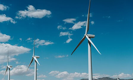 Two white wind turbines under a bright blue sky with scattered clouds.