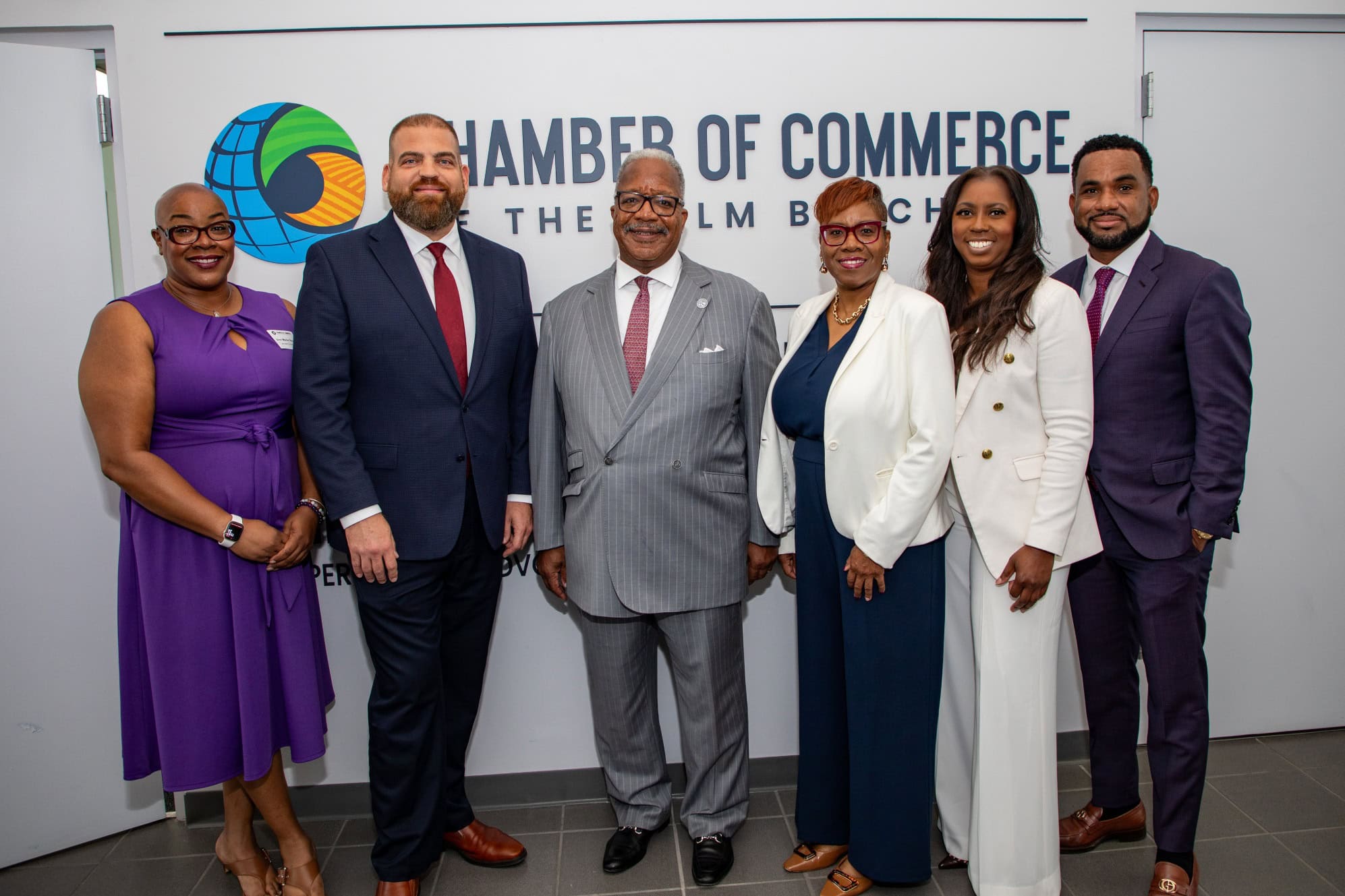 Group of six diverse professionals standing in front of Chamber of Commerce sign.