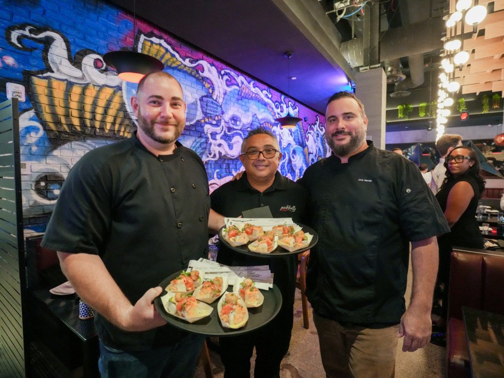 Three chefs holding plates of sushi in a vibrant restaurant setting.