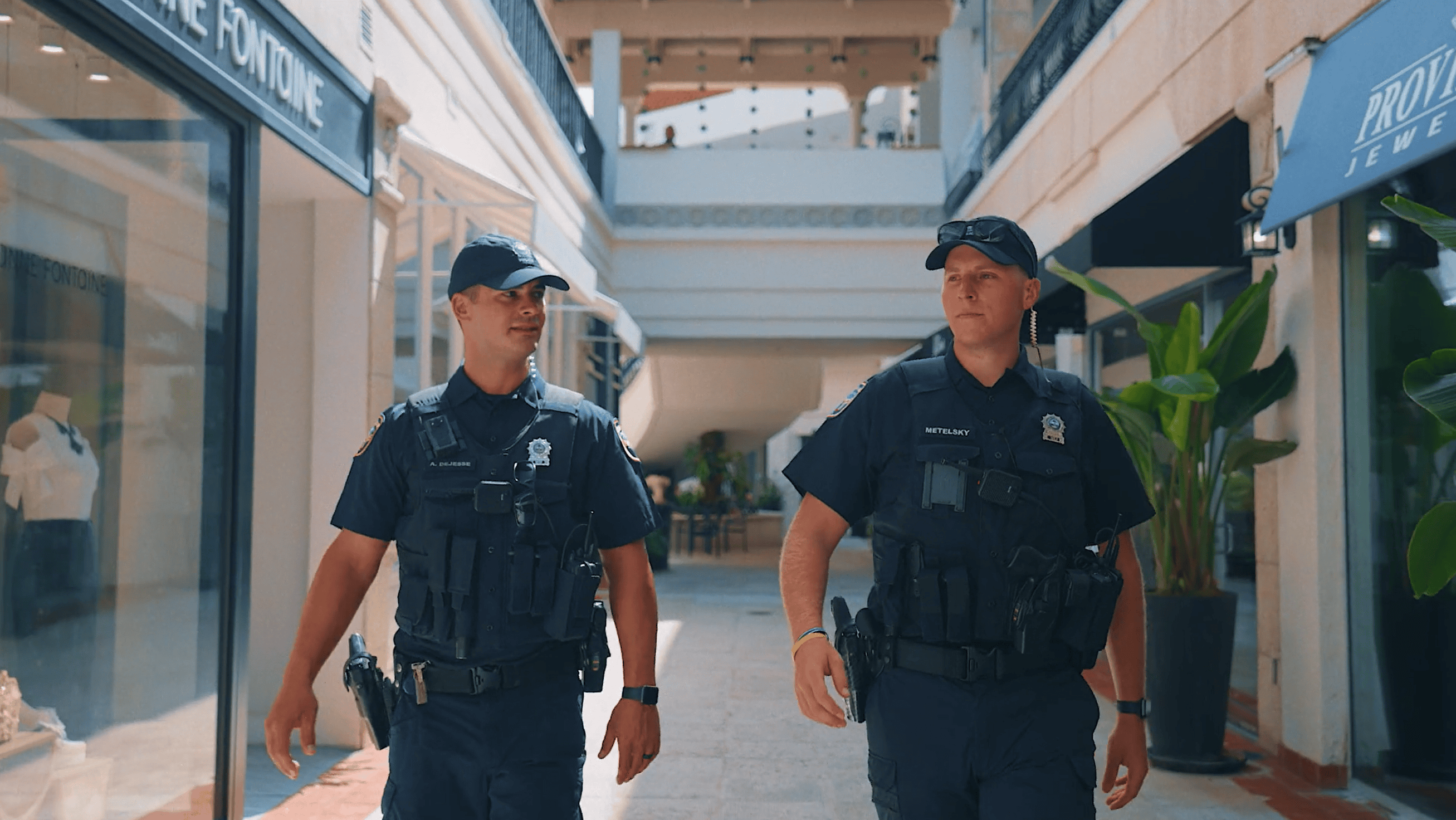 Two police officers walking in a shopping mall corridor with palm plants.