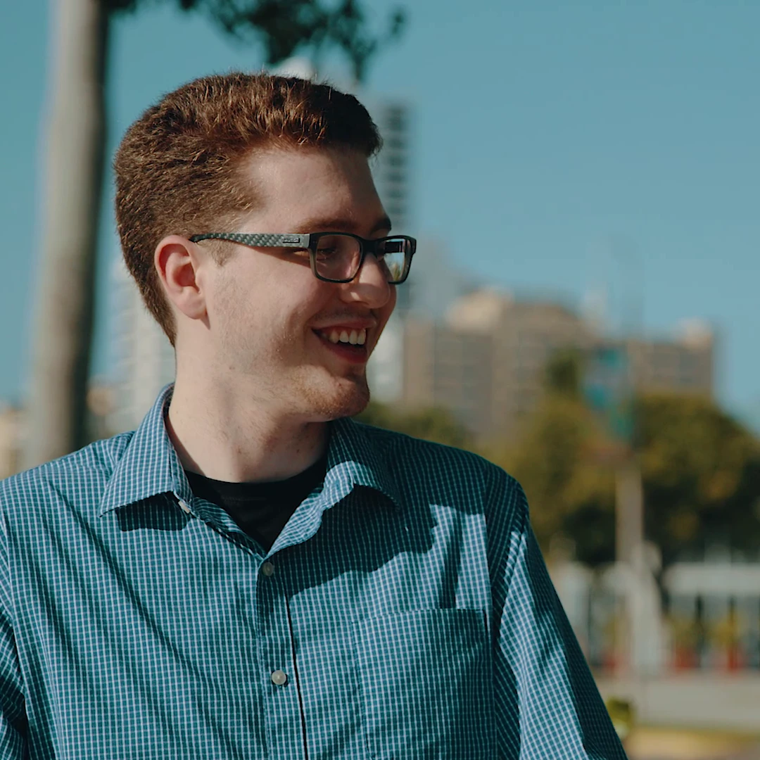 Smiling young man in blue checkered shirt outdoors in Palm Beach.