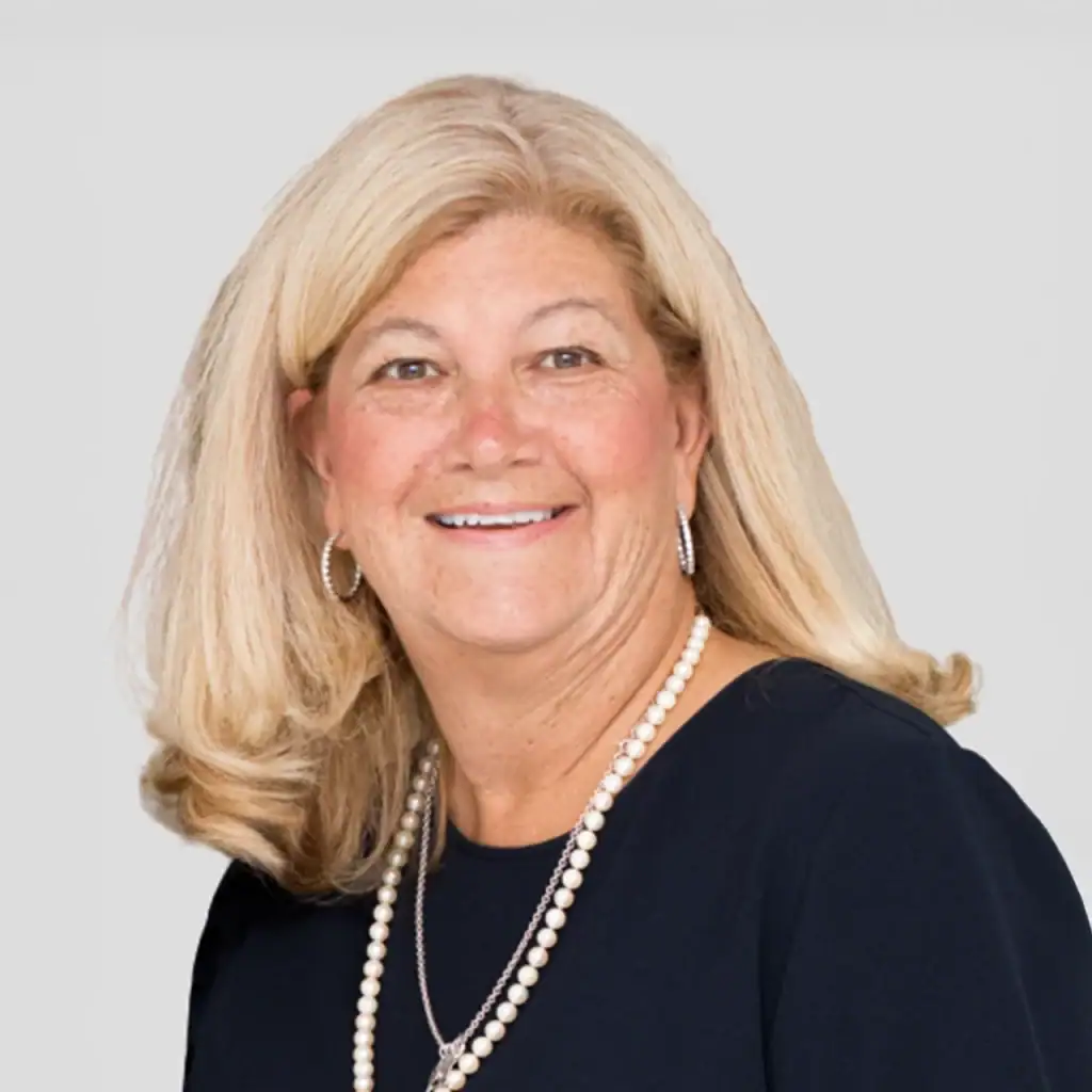 Portrait of a smiling woman with blonde hair wearing a navy blue top and pearl necklace.