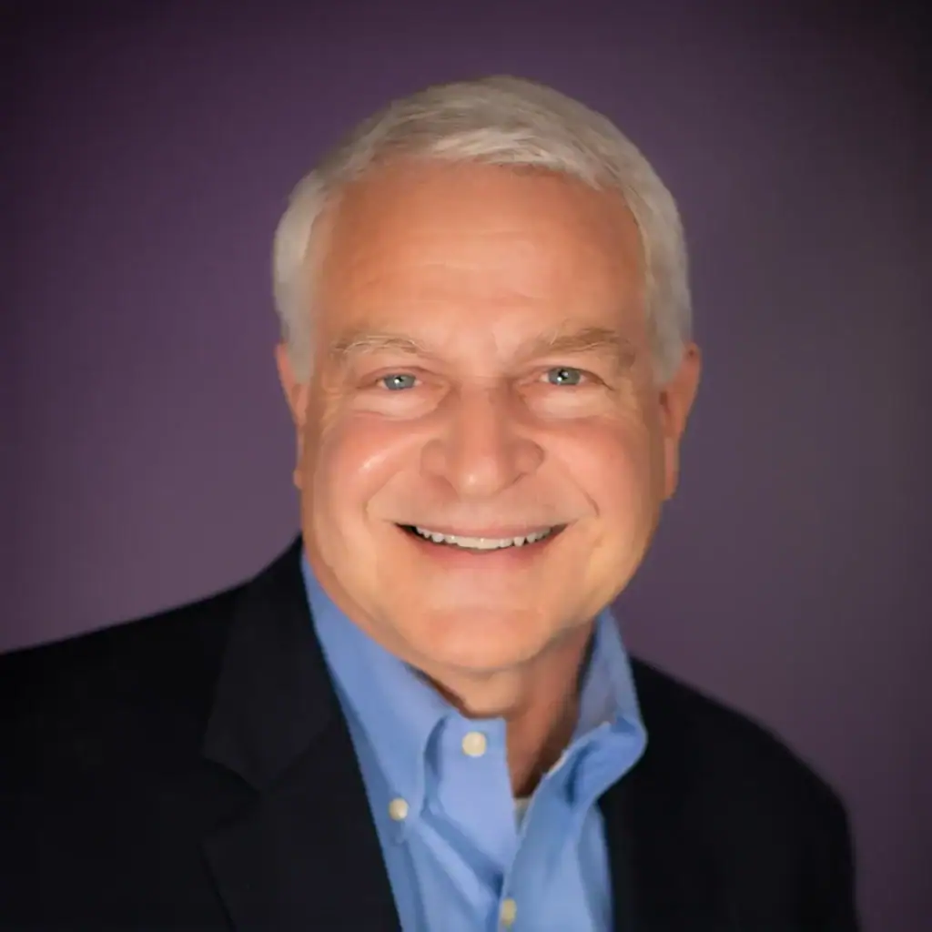Smiling man in a suit and blue shirt against purple background.