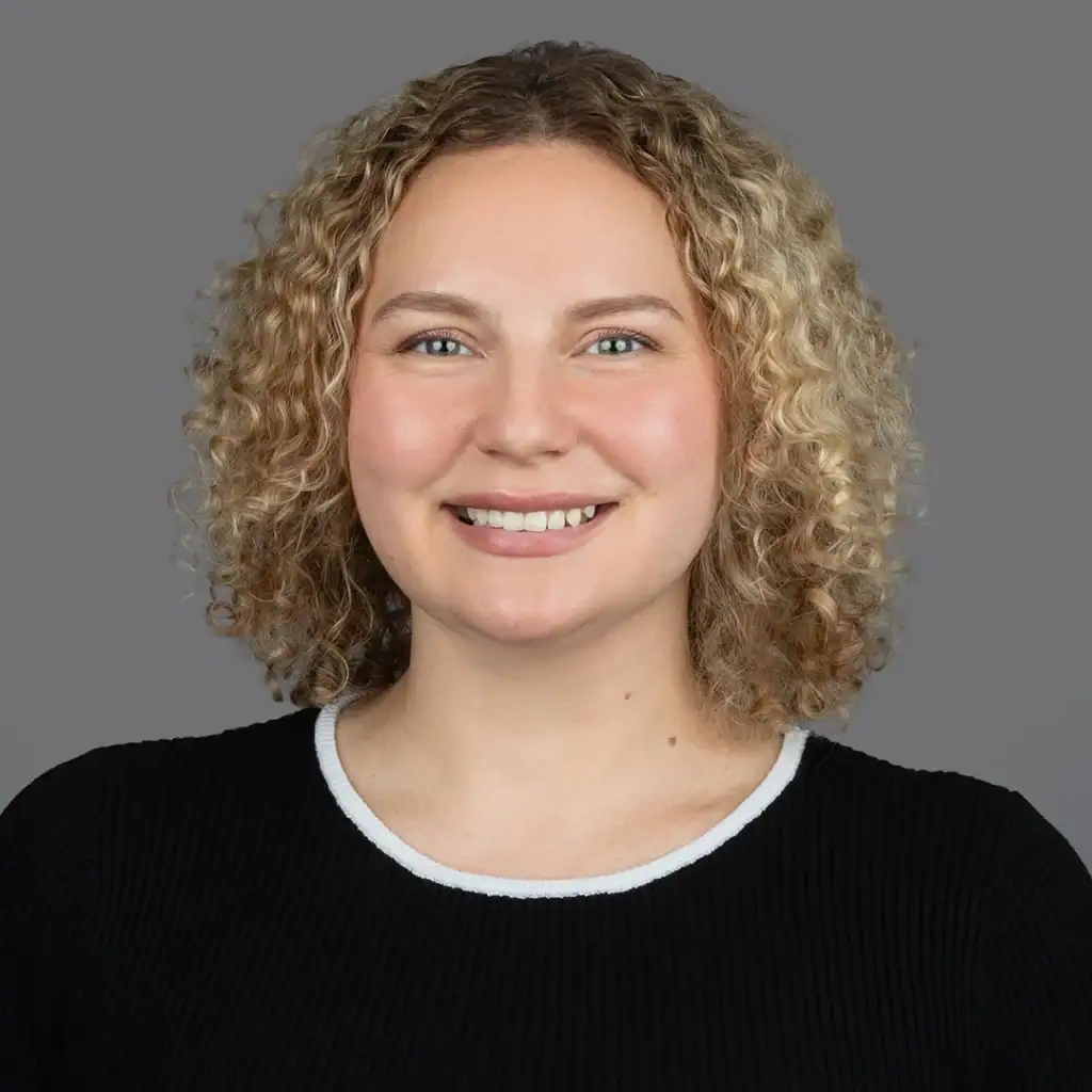 Smiling woman with curly blonde hair wearing a black top with white trim.